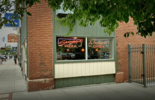 A corner restaurant with a neon sign reading "Sammy's Pizza & Restaurant Open" in a brick building.